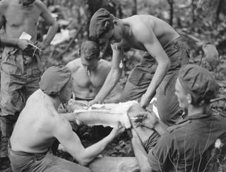 BOUGAINVILLE. 1945-05-24. STRETCHER BEARERS PLACING A SPLINT ON THE LEG OF SERGEANT V.C. ROBERTS (4), WHICH WAS BROKEN BY A JAPANESE BULLET WHILE ON A FIGHTING PATROL WITH D COMPANY, 58/59 INFANTRY ..