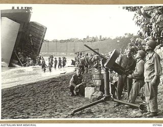 FINSCHHAFEN, NEW GUINEA. 1943-09-22. WHILE TROOPS OF THE FINSCHHAFEN FORCE UNLOAD STORES FROM THE LSTS (LANDING SHIP, TANK) THEY ARE PROTECTED BY A UNITED STATES ARMY GUN AND CREW IN THE FOREGROUND