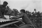 House-building: men attach corrugated metal roof