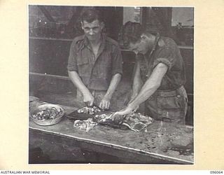 CAPE PUS, WEWAK AREA, NEW GUINEA. 1945-09-07. PRIVATE E.W. CONRAD (1), AND SAPPER A.J. MILTON (2), MEMBERS OF 2/14 FIELD COMPANY ROYAL AUSTRALIAN ENGINEERS, CUTTING UP STEAK FOR DINNER