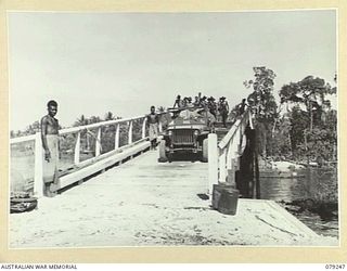 KALUMALAGI RIVER, NEW BRITAIN. 1945-02-13. THE JEEP OF THE 5TH DIVISION POSTAL UNIT MAKES HISTORY BY BEING THE FIRST VEHICLE TO CROSS THE NEW BRIDGE OVER THE RIVER