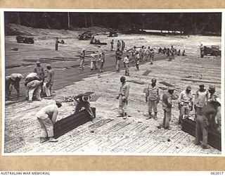 DREGER HARBOUR, NEW GUINEA. 1943-12-05. COLOURED ENGINEERS OF THE 870TH UNITES STATES AVIATION ENGINEER BATTALION LAYING STEEL MATTING AT THE SOUTH END OF THE NEW LANDING STRIP