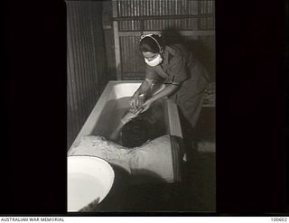 Lae, New Guinea. 1944-08-02. Sister M. E. Everett, treating a patient for burns at 2/7th Australian General Hospital. He is in a bath with his head supported