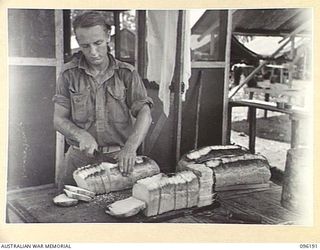 CAPE PUS, WEWAK AREA, NEW GUINEA, 1945-09-07. PRIVATE D.F. MILLER, 2/1 INFANTRY BATTALION, CUTTING UP LOAVES OF BREAD FOR THE MESS