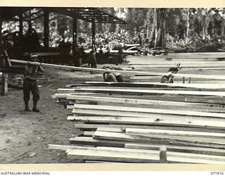 LAE, NEW GUINEA. 1944-03-30. N238785 SAPPER R.A. HOLMESBY (1), WITH N238782 SAPPER M.V. GREEN (2), STACKING MILLED TIMBER AT THE 59TH CORPS FIELD PARK COMPANY. THE TIMBER IS CARTED TO UNITS FOR ..