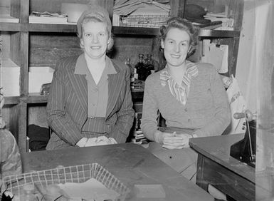 [Portrait of two women seated in front of tables or desks]