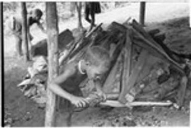 Child getting coal burning for pipe, leaf oven cooking in background