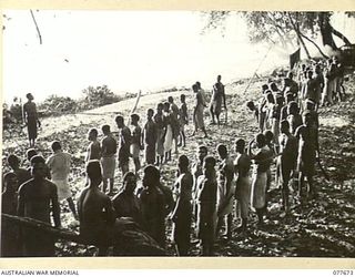 JACQUINOT BAY, NEW BRITAIN. 1944-12-13. NATIVES STANDING EASY ON THE BEACH AFTER THE MORNING ROLL CALL AT THE AUSTRALIAN NEW GUINEA ADMINISTRATIVE UNIT NATIVE COMPOUND NEAR THE MOUTH OF THE MALOPI ..