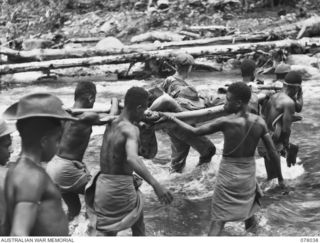 BOUGAINVILLE ISLAND. 1944-12-31. PRIVATE HARRIS, REGIMENTAL AID POST ORDERLY, SUPERVISING NATIVE STRETCHER BEARERS AS THEY CARRY N130284 PRIVATE KERWICK ACROSS THE LARUMA RIVER DURING THE ATTACK ON ..