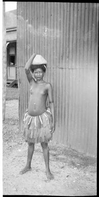 Young girl wearing a grass skirt with a parcel of sago on her head, Awar, Sepik River, New Guinea, 1935, 2 / Sarah Chinnery