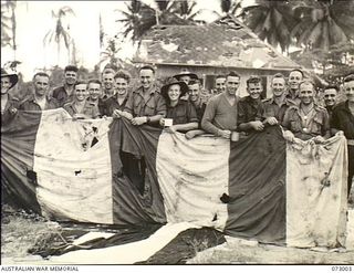 Madang, New Guinea. 1944-04-25. Personnel at Headquarters 8th Infantry Brigade hold the remnants of a Japanese "dropping flag" used to indicate the site for messages dropped by Japanese aircraft. ..