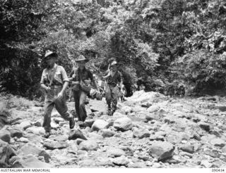 WONGINARA MISSION, NEW GUINEA. 1945-04-04. SERGEANT L.V. NICHOLLS OF AUSTRALIAN NEW GUINEA ADMINISTRATIVE UNIT (1), WITH A NATIVE SUPPLY LINE ESCORTED BY 2/3 INFANTRY BATTALION PERSONNEL AS FOOD IS ..