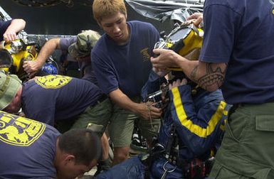Onboard the Crowley 450-10 barge, US Navy (USN) divers assigned to Mobile Diving and Salvage Unit One (MDSU-1) and Japanese Self Defense Force divers, help a team of divers remove their gear after returning from a dive, during recovery operations for the Japanese fishing vessel Ehime Maru off the coast of Hawaii