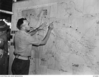 LAE-NADZAB, NEW GUINEA. 1944-07-20. NGX369 CAPTAIN N. OWERS, INTELLIGENCE OFFICER, CHIEF ENGINEERS BRANCH STUDYING A WALL MAP IN THE ENGINEER INTELLIGENCE ROOM AT HEADQUARTERS, NEW GUINEA FORCE