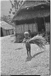 Young child with bundle of long grass, by government rest house in Tsembaga, anticipating patrol officer's visit