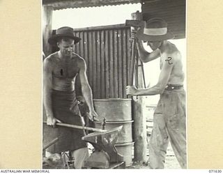 LAE, NEW GUINEA. 1944-03-24. QX8581 CRAFTSMAN (CFN) C. W. JOHNSTON (1), WITH QX9608 CFN M. A. HARRISON (2), SHAPING IRON ON AN ANVIL AT THE BLACKSMITH'S SHOP AT 2/125TH BRIGADE WORKSHOP ATTACHED TO ..
