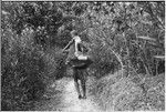 Young child stands on firewood carried in netbag by a woman