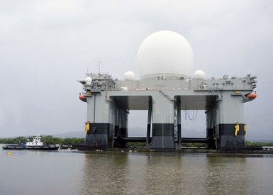 The Sea Based X-Band Radar (SBX) is assisted by a commercial tugboat, as it departs Pearl Harbor, Hawaii (HI) after a three-month port visit. The SBX arrived to undergo minor modifications, post-transit maintenance and routine inspections. The on-board propulsion system allows SBX to transit to its homeport in Adak, Alaska in the Aleutian Islands. The SBX will provide the nation with highly advanced ballistic-missile detection