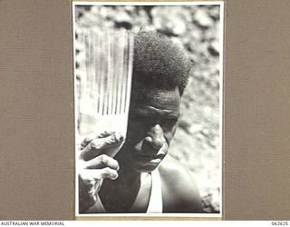 LALOKI RIVER, NEW GUINEA. 1944-01-02. A POLICE BOY TRYING OUT A NEW COMB WHICH HE HAS WHITTLED FROM A PIECE OF WOOD