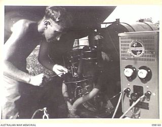 WEWAK POINT, NEW GUINEA. 1945-10-23. CORPORAL F.W. WIGGINS, A MEMBER OF THE STAFF OF RADIO STATION 9AJ, 1 BROADCASTING STATION, AUSTRALIAN ARMY AMENITIES SERVICE, WHO IS IN CHARGE OF THE GENERATOR ..