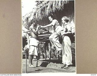 NEW GUINEA. 1943-11-17. MEMBERS OF THE AUSTRALIAN ARMY MEDICAL WOMEN'S SERVICE (AAMWS) DELL POWER OF TOOWOOMBA, QLD AND JEANNINE LEWIS OF POTTS POINT, NSW WATCH A LOCAL, NAGADA, MAKE REPAIRS TO HIS ..