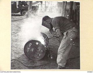 BORAM BEACH, WEWAK AREA, NEW GUINEA. VX30265 WARRANT OFFICER 2 ALAN THOMAS BALLINGALL, 2/41 LIGHT AID DETACHMENT, CORPS OF AUSTRALIAN ELECTRICAL AND MECHANICAL ENGINEERS, CUTTING A 44 GALLON DRUM ..