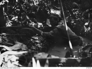 BOUGAINVILLE ISLAND. 1945-01-21. V514074 PRIVATE R.A. VIGENSER IN HIS WATER-FILLED DUGOUT COVERING AN AREA WHERE JAPANESE RAIDERS COULD MOVE IN AGAIN AND INFLICT CASUALTIES ON MEMBERS OF THE 42ND ..