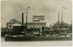 Bundaberg Distiller [on the banks of the Burnett River], showing the distillery building and a ship in the foreground, Bundaberg