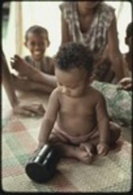 Infant on woven mat plays with canister