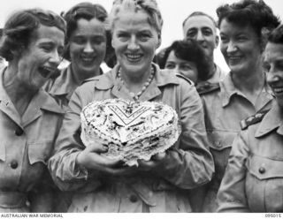 LAE AREA, NEW GUINEA. 1945-08-19. GRACIE FIELDS, WITH MEMBERS OF THE SISTERS' MESS, AUSTRALIAN ARMY NURSING SERVICE, 2/8 GENERAL HOSPITAL, HOLDING A CAKE PRESENTED TO HER BY THE CANTEEN STAFF
