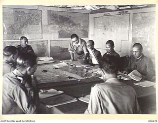 CAPE WOM, NEW GUINEA, 1945-09-13. GENERAL DISCUSSION AT COMMENCEMENT OF A CONFERENCE BETWEEN STAFF OFFICERS OF 6 DIVISION, HEADED BY LIEUTENANT-COLONEL J. BISHOP, GENERAL STAFF OFFICER I, AND STAFF ..