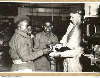 ALEXANDRIA, NSW. 1944-01-24. AUSTRALIAN AND NEW GUINEA ADMINISTRATION UNIT NATIVES INSPECTING A PARTLY FINISHED WOODEN BARRELL CRADLE AT THE SLAZENGER'S FACTORY