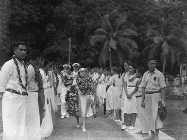 [Woman leading Navy personnel through rows of Pacific Islanders]