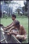 Canoe-building: men use lengths of vine to lash outrigger frame to a canoe