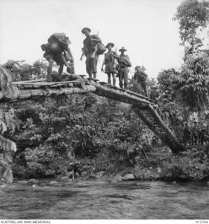 1942-12-01. NEW GUINEA. ON THE WAY TO WAIROPI. AUSTRALIAN TROOPS CROSS ONE OF THE MANY STREAMS ON A RICKETY PATCHWORK BRIDGE. (NEGATIVE BY G. SILK)