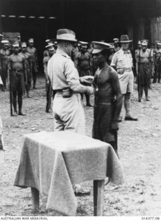 1943-03-03. PRESENTATION OF LOYAL SERVICE MEDALS AT WAU AERODROME. ONE OF THE FOUR NATIVE CONSTABLES DECORATED FOR LOYAL SERVICE RECEIVES HIS MEDAL FROM THE G.O.C. NEW GUINEA FORCES. THE CEREMONY ..