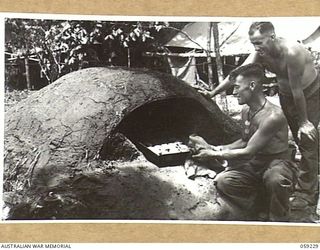 DUMPU, NEW GUINEA, 1943-10-23. SX12340 PRIVATE S.L. MORGAN (1), A COOK AT HEADQUARTERS, 7TH AUSTRALIAN DIVISION, TAKING A BATCH OF SCONES FROM AN ALDERSHOT OVEN