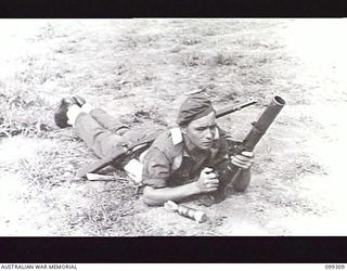 RABAUL, NEW BRITAIN, 1945-12-06. A SOLDIER HOLDING A 2-INCH MORTAR IN ITS FIRING POSITION DURING A DEMONSTRATION OF VARIOUS INFANTRY WEAPONS AND EQUIPMENT