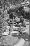 Distribution of wild pig meat: man cuts cooked pork, closely watched by children