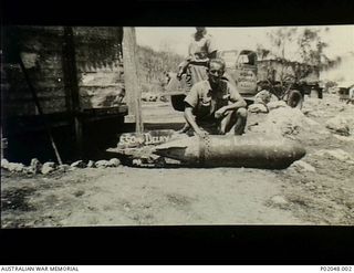 Port Moresby, New Guinea. 1943. An unidentified member of a RAAF Bomb Disposal Unit kneeling behind a 550 lb (250 kg) delay action bomb labelled "Bad luck Tojo", a message to the Japanese General. ..
