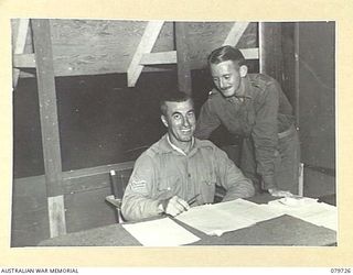 BOSLEY FIELD, BOUGAINVILLE, SOLOMON ISLANDS. 1945-03-15. QX30229 SERGEANT A. ST.GEORGE OF TOWNSVILLE, QLD, STATION MANAGER, AUSTRALIAN ARMY BROADCASTING STATION (1), DISCUSSING SCRIPT WITH ..