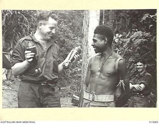 1943-09-14. NEW GUINEA. KOMIATUM RIDGE. PTE. FRED MARTIN OF DUNEDO, N.S.W., SHOWS A NATIVE CARRIER, DARSU, THREE-INCH SHELLS LEFT BEHIND BY THE JAPANESE WHEN THEY ABANDONED KOMIATUM RIDGE. ..