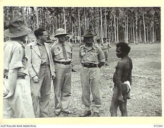 MILNE BAY, NEW GUINEA. 1944-04-20. THE HONOURABLE E.J. WARD (2), MINISTER FOR EXTERNAL TERRITORIES IN THE AUSTRALIAN GOVERNMENT, WITH MEMBERS OF THE OFFICIAL PARTY, AND ONE OF THE MORE INFAMOUS ..