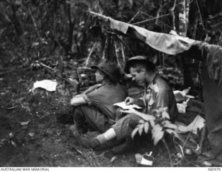 SATTELBERG AREA, NEW GUINEA. 1943-11-15. VX31364 PRIVATE T. W. HARGREAVES WRITES A LETTER HOME WHILE NX83143 CORPORAL T. DICK KEEPS A LOOK OUT AT ONE OF THE ADVANCE MACHINE GUN POSTS OF THE 2/24TH. ..