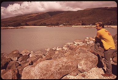 AT PUKOO DEVELOPMENT SITE, BRUCE BOWEN, ISLAND RESIDENT SCHOOL TEACHER, AND PART-TIME NEWSPAPER PUBLISHER, STUDIES THE MAN-MADE SHORE. BOWEN IS CONDUCTING A ONE MAN CAMPAIGN TO SLOW DOWN DEVELOPMENT ON THE ISLAND