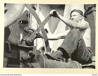 HOSKINS, NEW BRITAIN. 1944-10-08. QX8204 SAPPER S. THOMPSON, A WINCHMAN OF THE 2/31ST DOCK OPERATING COMPANY OPERATING ONE OF THE WINCHES ABOARD THE DUTCH TROOPS SHIP "SWARTENHONDT", WHICH BROUGHT ..