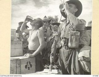 MADANG, NEW GUINEA. 1944-04-24. TROOPS OF THE 5TH DIVISION DRINKING FROM TINS OF ORANGE JUICE AT A DETAIL ISSUE DEPOT