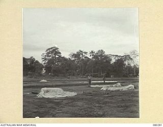 NADZAB, NEW GUINEA. 1944-10-21. PERSONNEL AT HEADQUARTERS NEW GUINEA FORCE EXAMINE THE CLOSE PROXIMITY OF DROPPED SUPPLIES TO THE TARGET, (COLOURED PARACHUTE AT THE CENTRE OF THE PHOTOGRAPH)