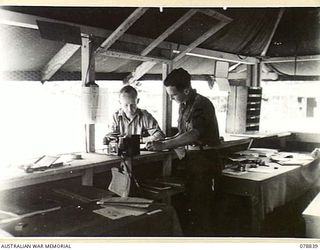 TOROKINA, BOUGAINVILLE ISLAND. 1945-01-30. VX87680 CORPORAL W.J. WALKER (1) AND VX87691 SERGEANT E.G. WILLIAMS (2) OF THE 4TH SUPPLY DEPOT PLATOON CHECKING LISTS OF SUPPLIES IN THE UNIT OFFICE