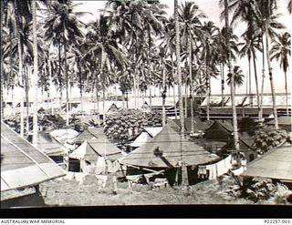 Astrolabe Bay, Madang, New Guinea, c. 1944. Nestling among tropical palm trees are buildings and tents of Headquarters, RAAF Northern Command (NORCOM). In the foreground are the tents of the RAAF ..